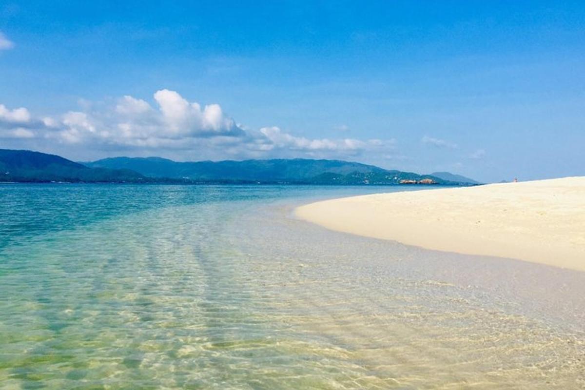 Una playa con agua clara y montañas al fondo.