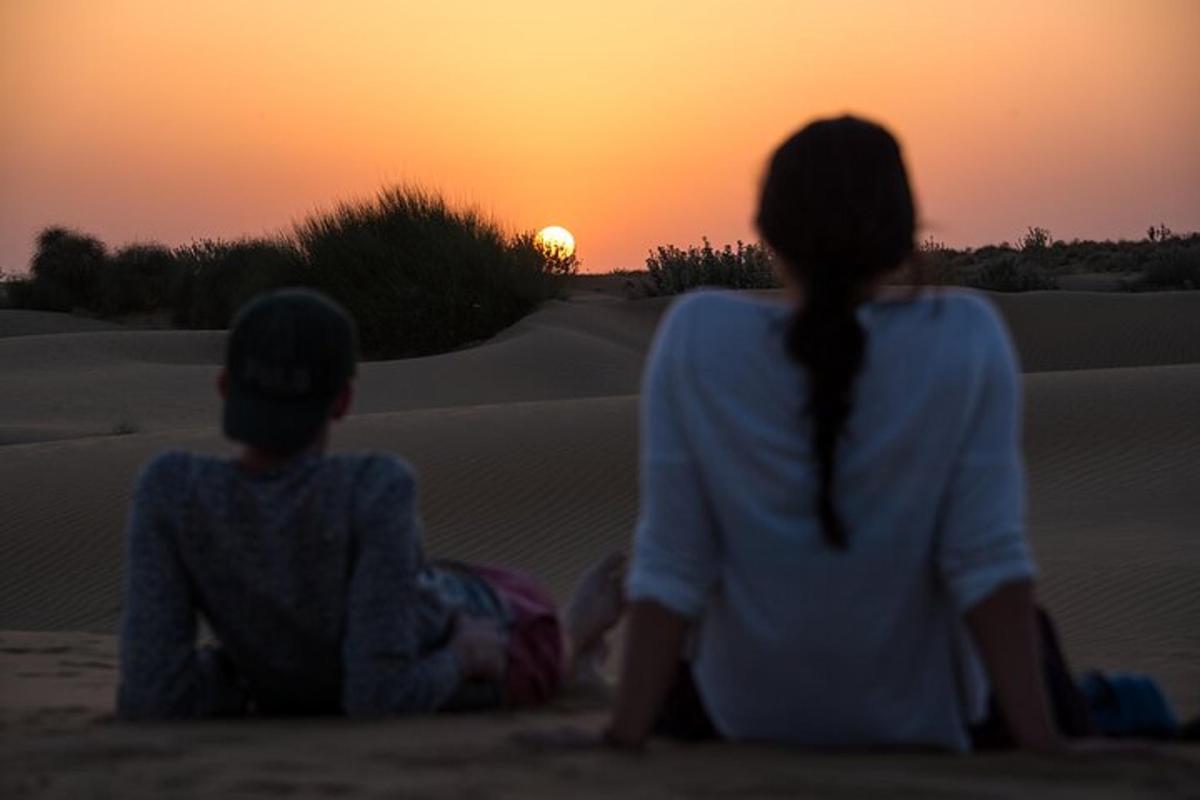 two people sitting in the desert watching the sunset