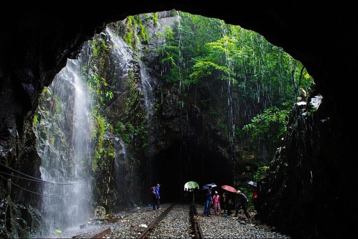 a group of people with umbrellas standing in front of a waterfall
