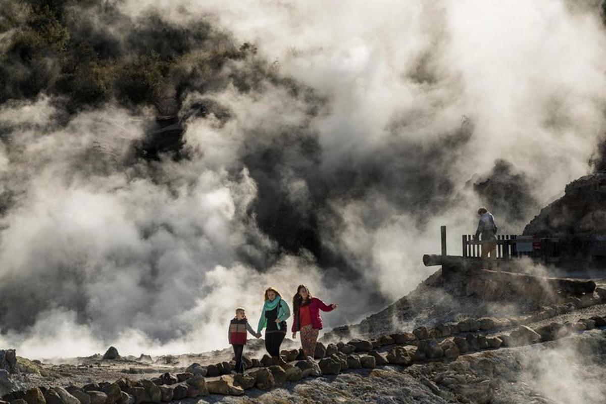 three people walking on a rock ledge with steam in the background