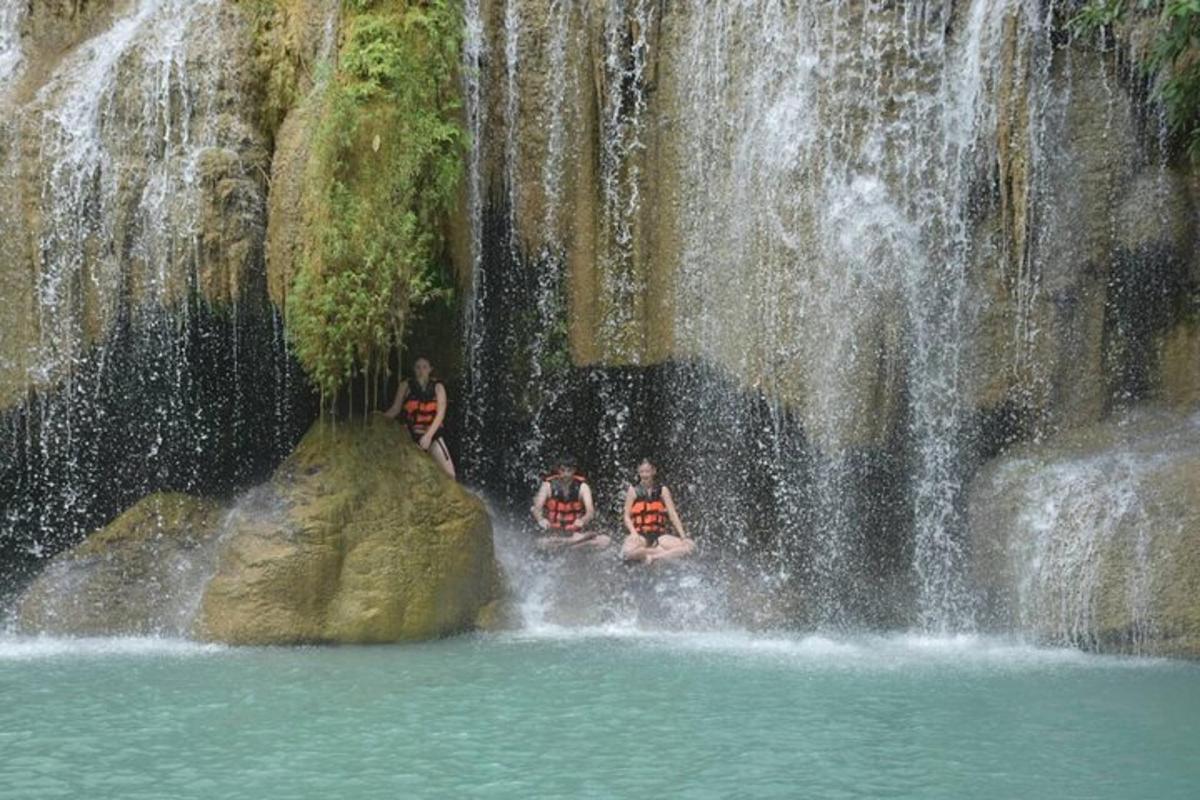Tres personas sentadas en las rocas frente a una cascada