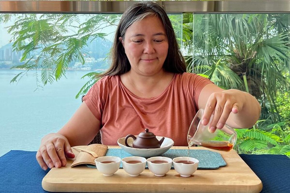 uma mulher sentada à mesa com uma bandeja de xícaras de chá