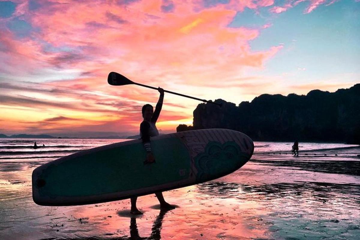 una persona che tiene una pagaia sulla spiaggia con una tavola da surf