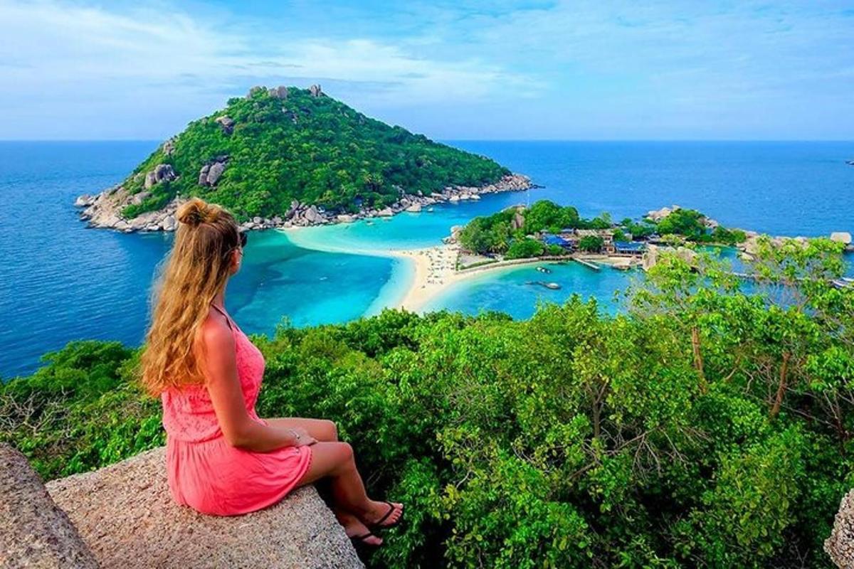 Una mujer sentada en el borde de un acantilado con vistas a una playa.