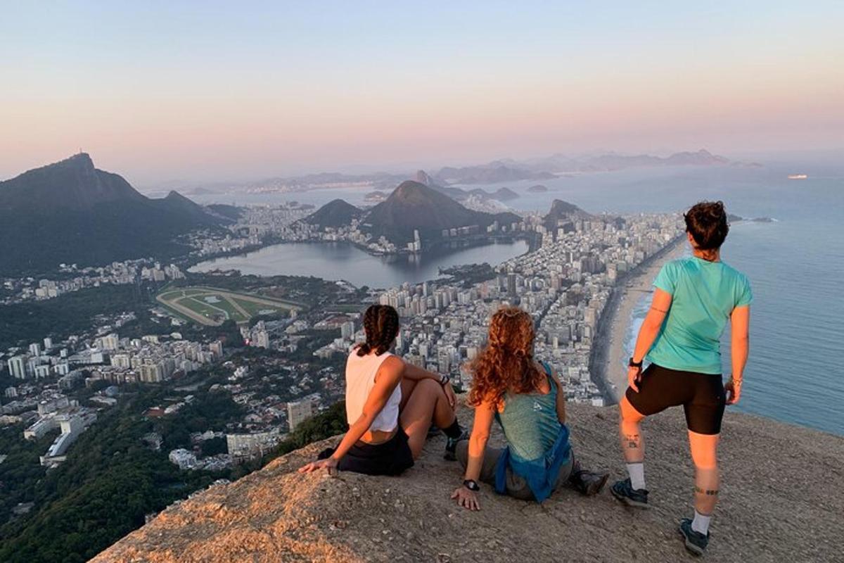 três pessoas sentadas no topo de uma montanha com vista para uma cidade