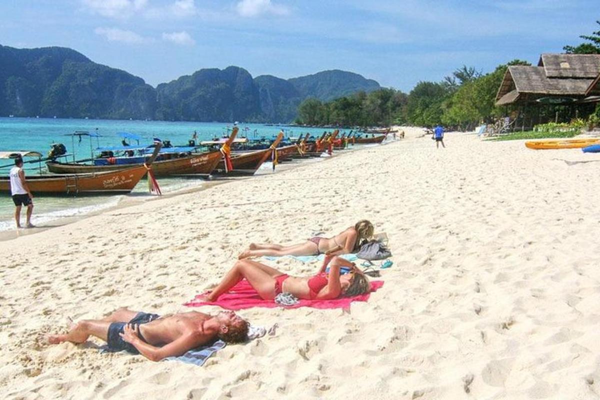 due persone sdraiate su asciugamani su una spiaggia con barche