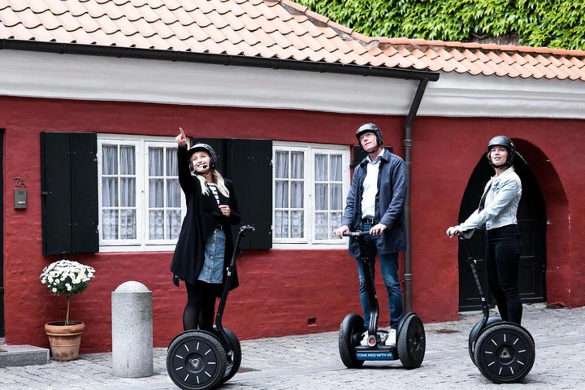tři lidé jedoucí na segwayích před červenou budovou