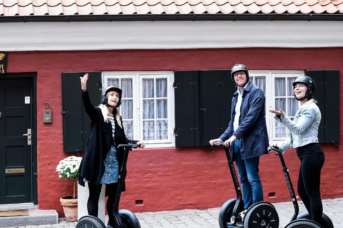 Skupina tří lidí jedoucích na segwayích před červenou budovou