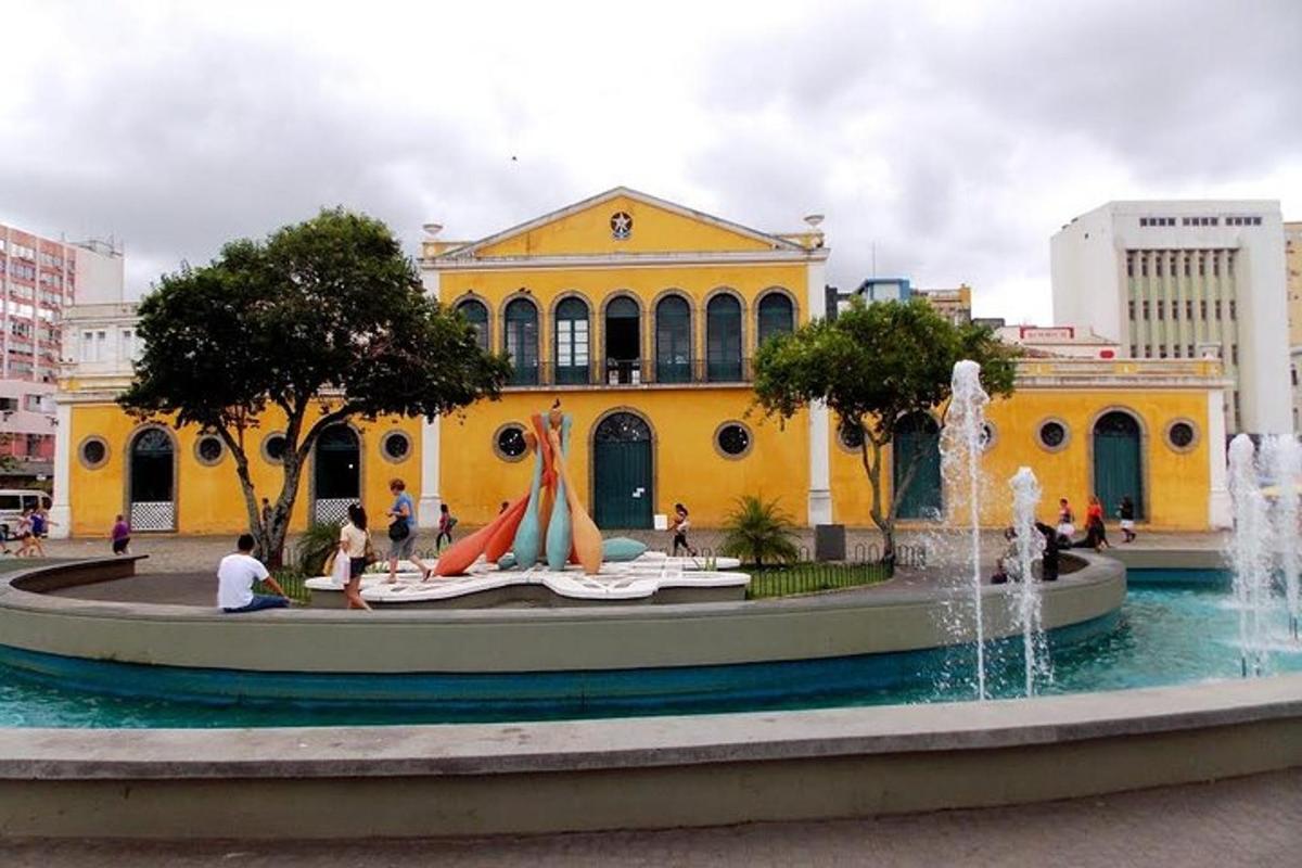 a yellow building with people sitting in front of a fountain