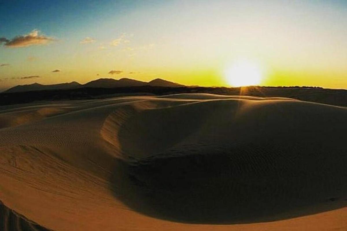 a sunset over a desert with the sun setting in the background