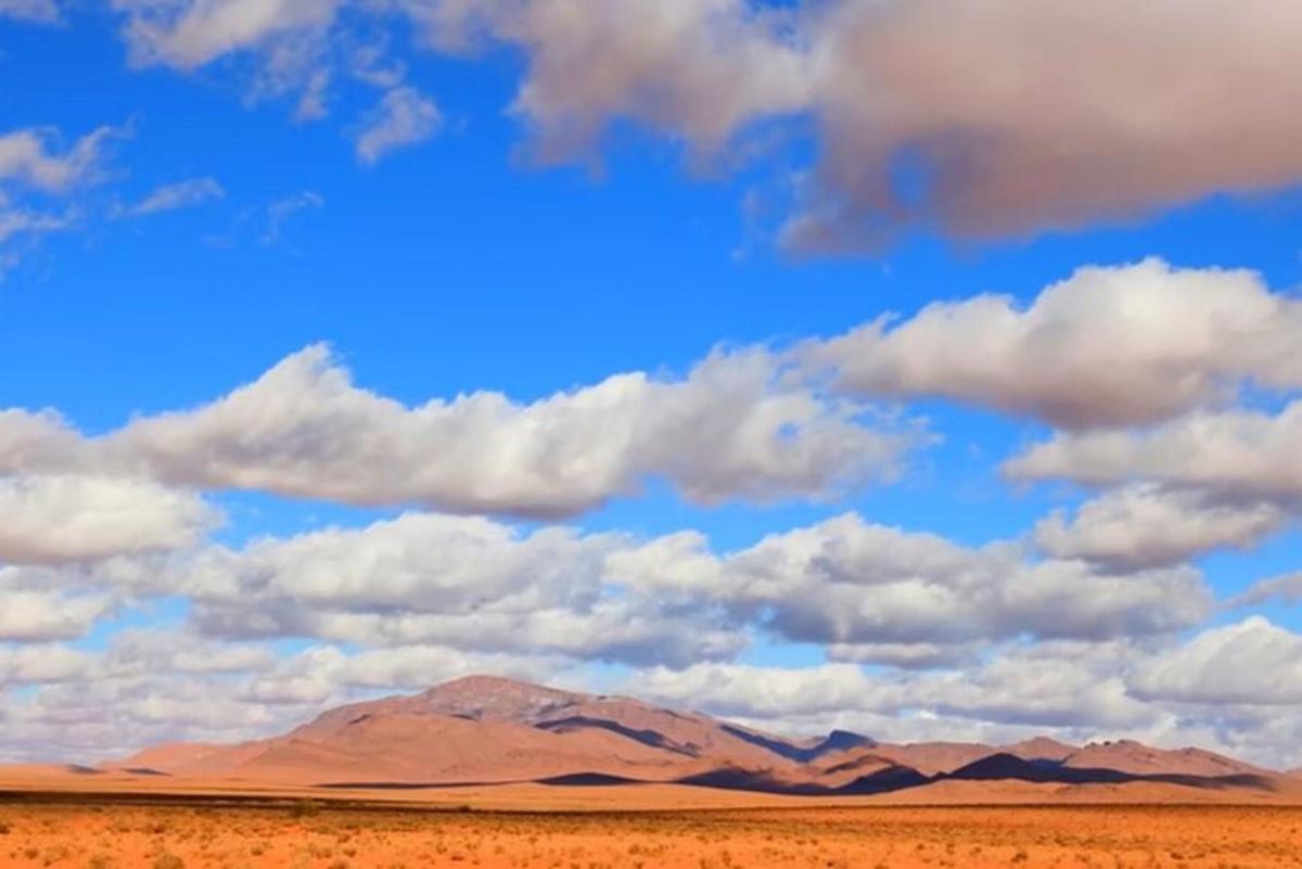 a view of a desert with a cloudy sky and mountains