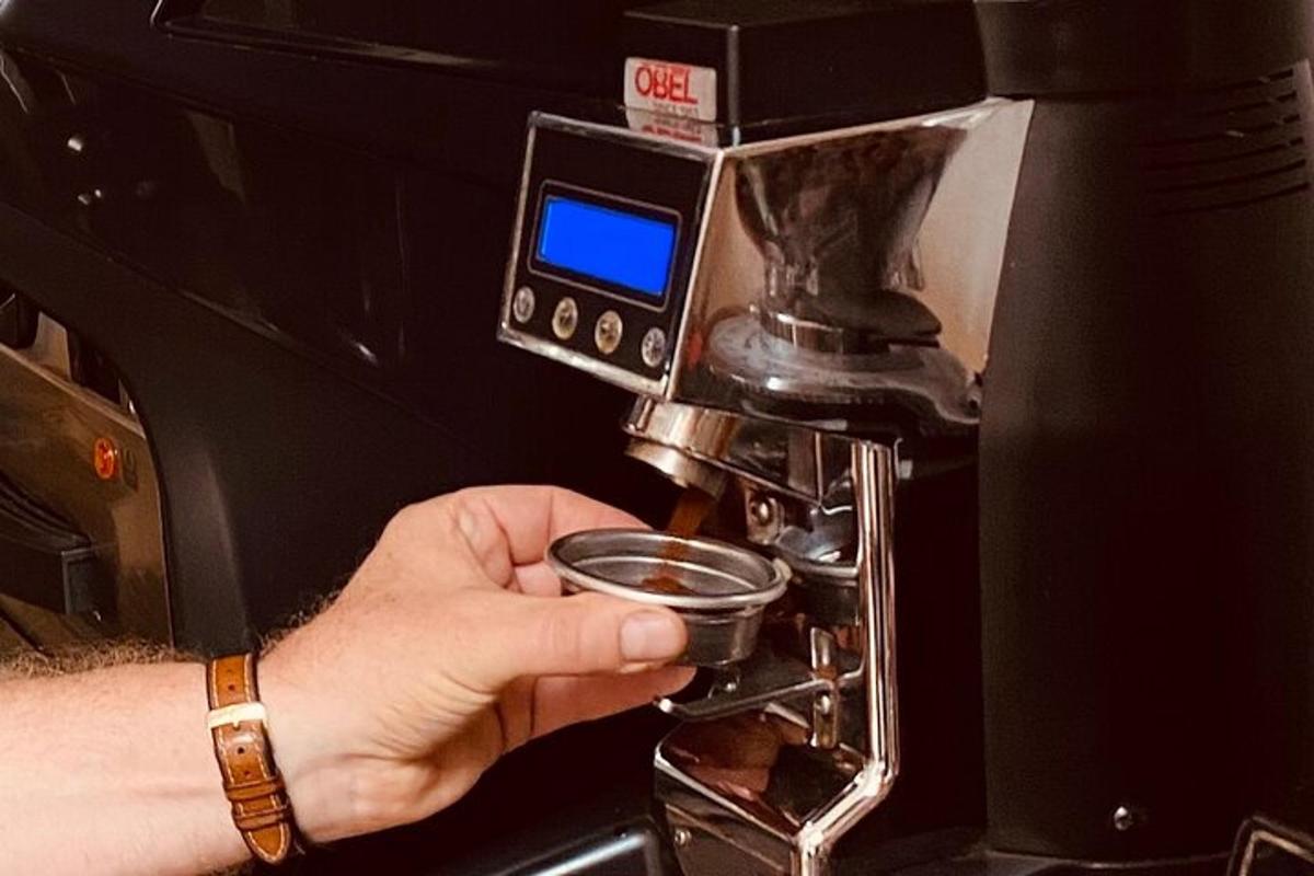 cilvēks tur krūzi kafijas automāta priekšā