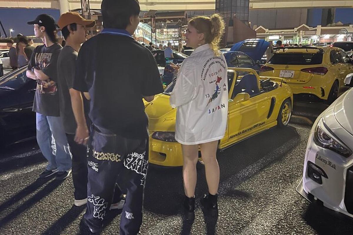 Una mujer está parada junto a un coche amarillo.