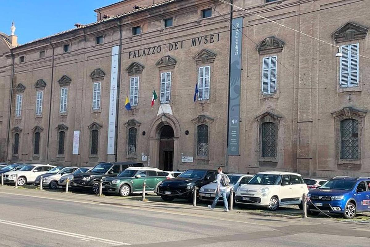 čovjek sjedi ispred zgrade s parkiranim automobilima ispred