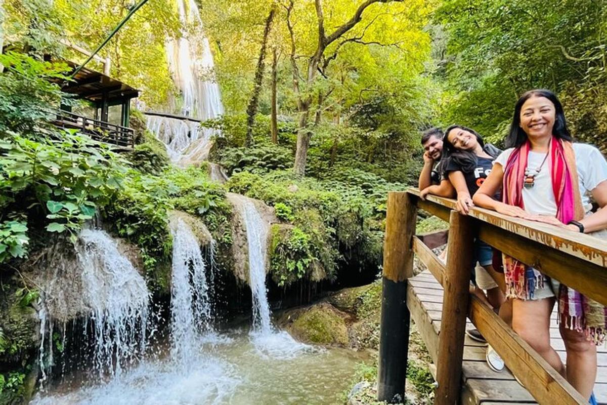three people sitting on a bridge near a waterfall