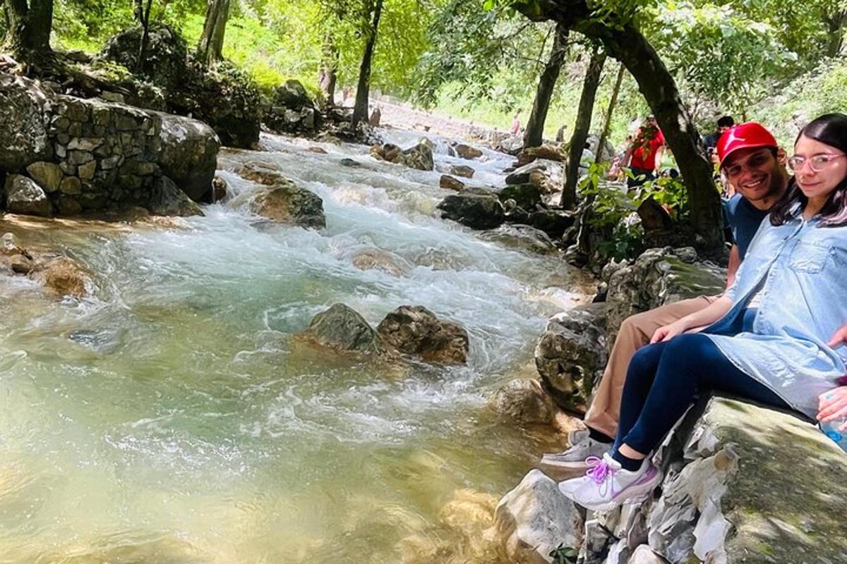 two people sitting on rocks next to a stream