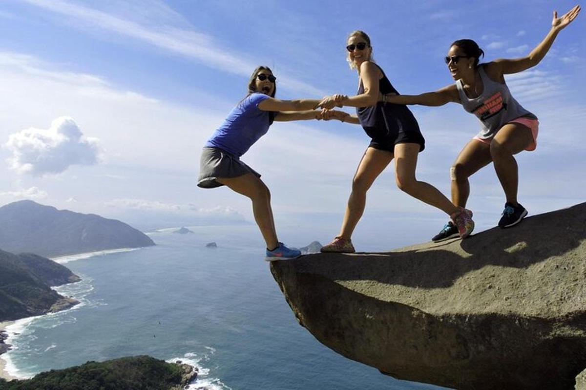 três mulheres em pé no topo de uma rocha com vista para o oceano