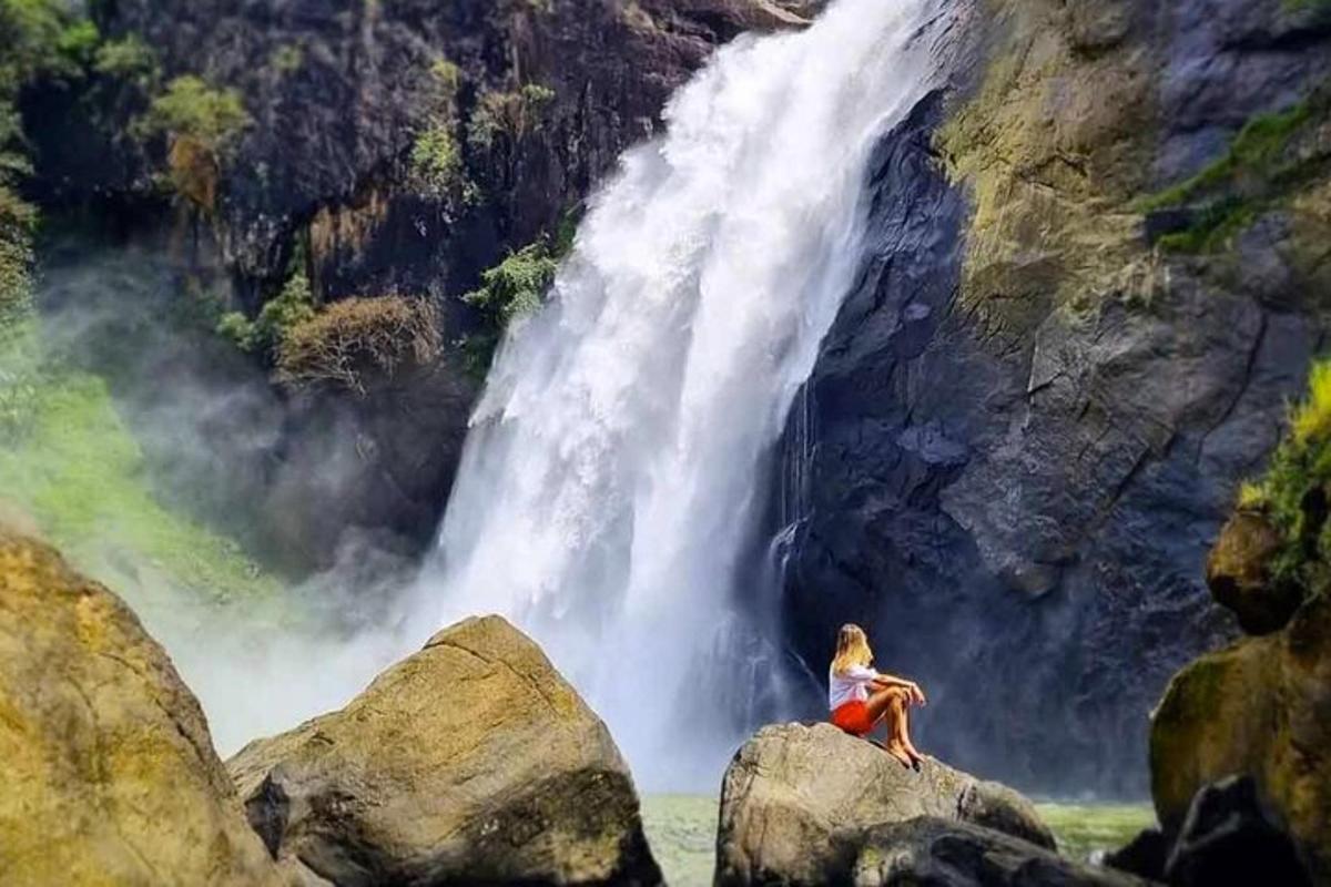 uma mulher sentada em uma rocha em frente a uma cachoeira