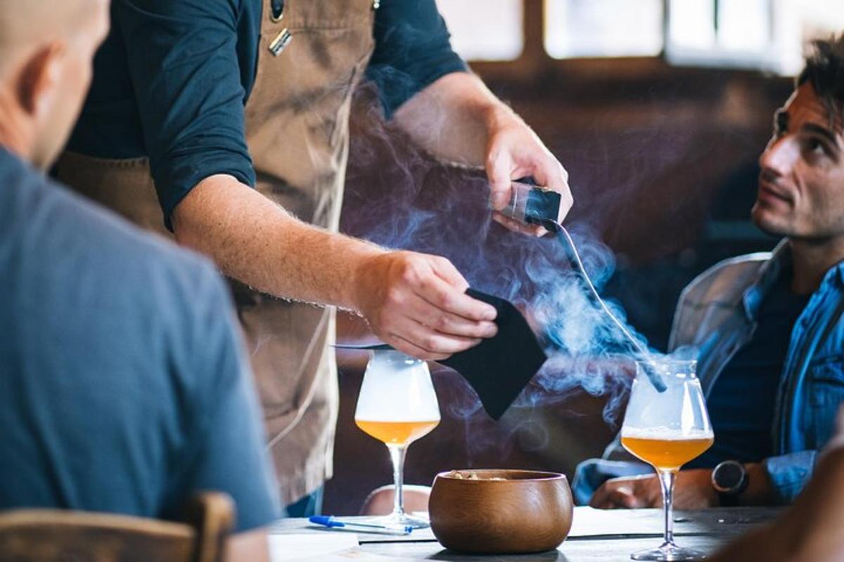 a man cooking a drink in a table with people sitting around