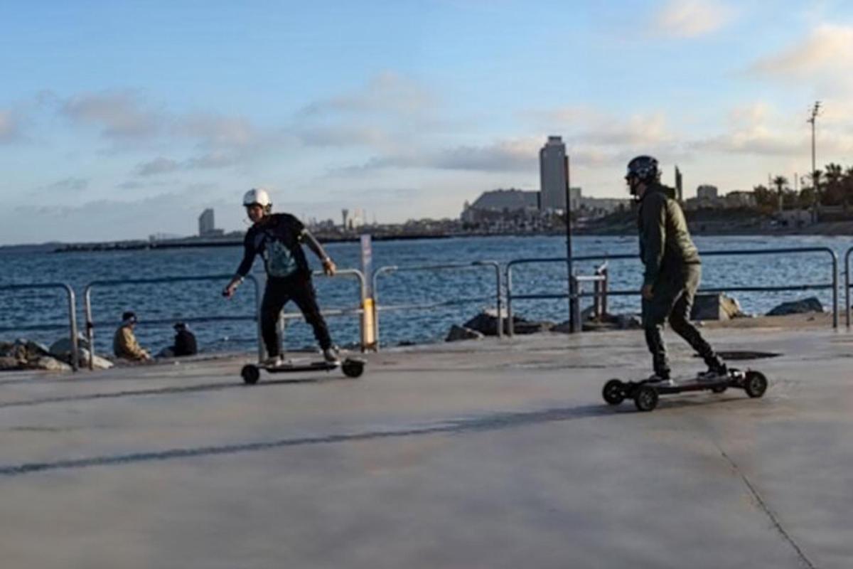 doi bărbați mergând pe skateboard pe un trotuar lângă apă
