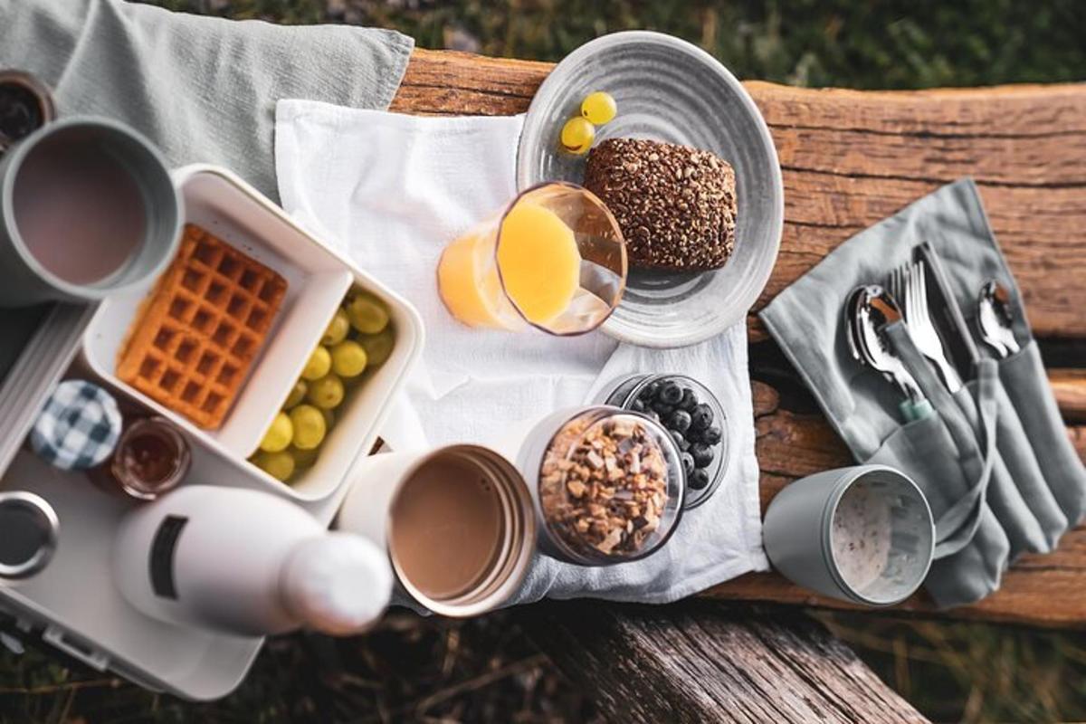 un tavolo da picnic con cibo per la colazione, tazze e utensili