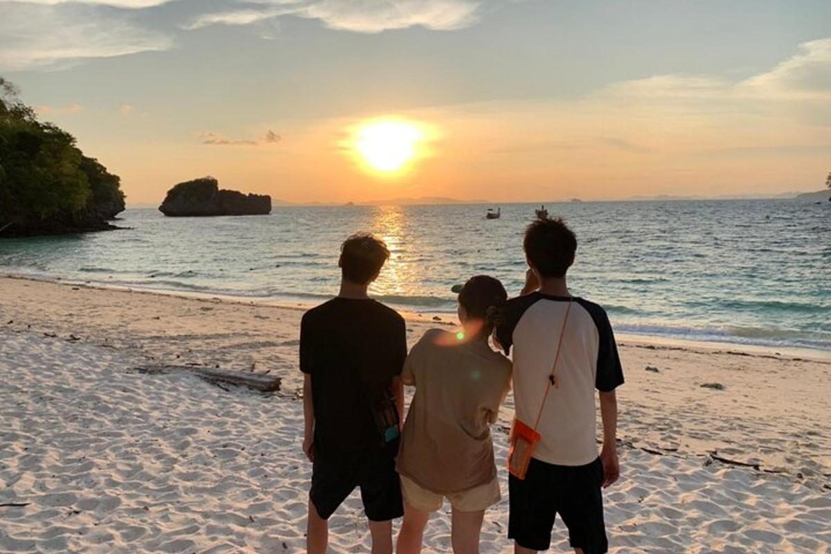 sekumpulan tiga orang berdiri di pantai melihat matahari terbenam