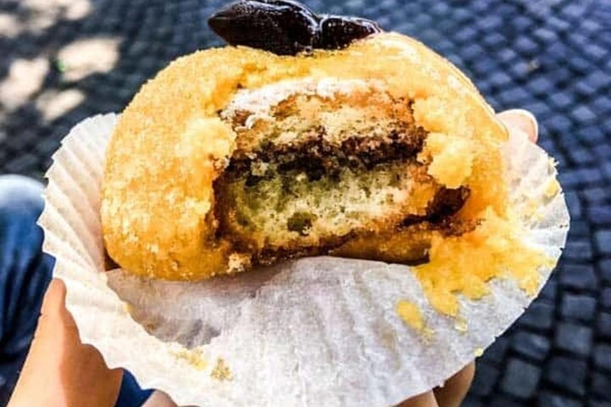 una persona tiene in mano una ciambella con ripieno di mirtilli