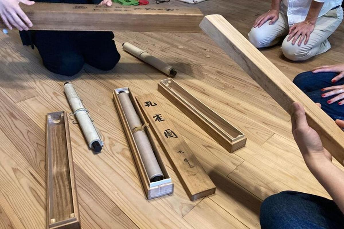 grupė žmonių, sėdinčių ant grindų su medinėmis lazdomis