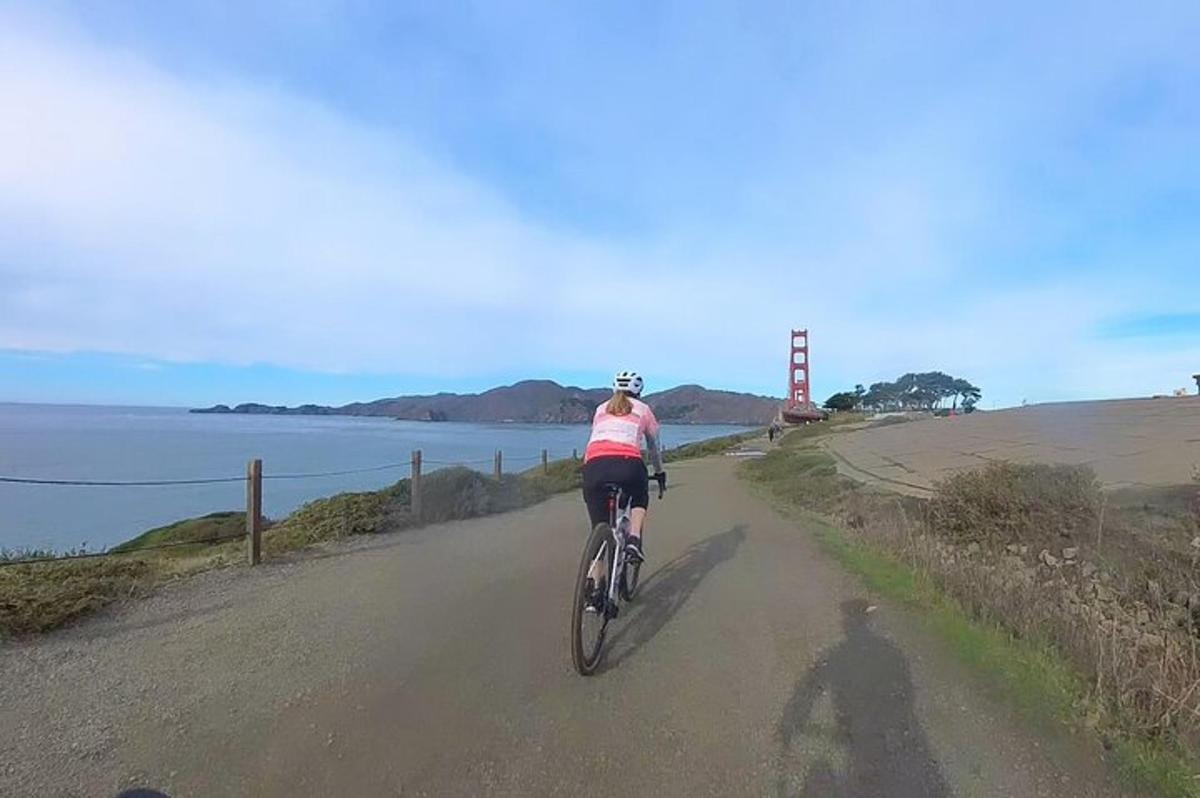 Žena jedoucí na kole po silnici s mostem Golden Gate