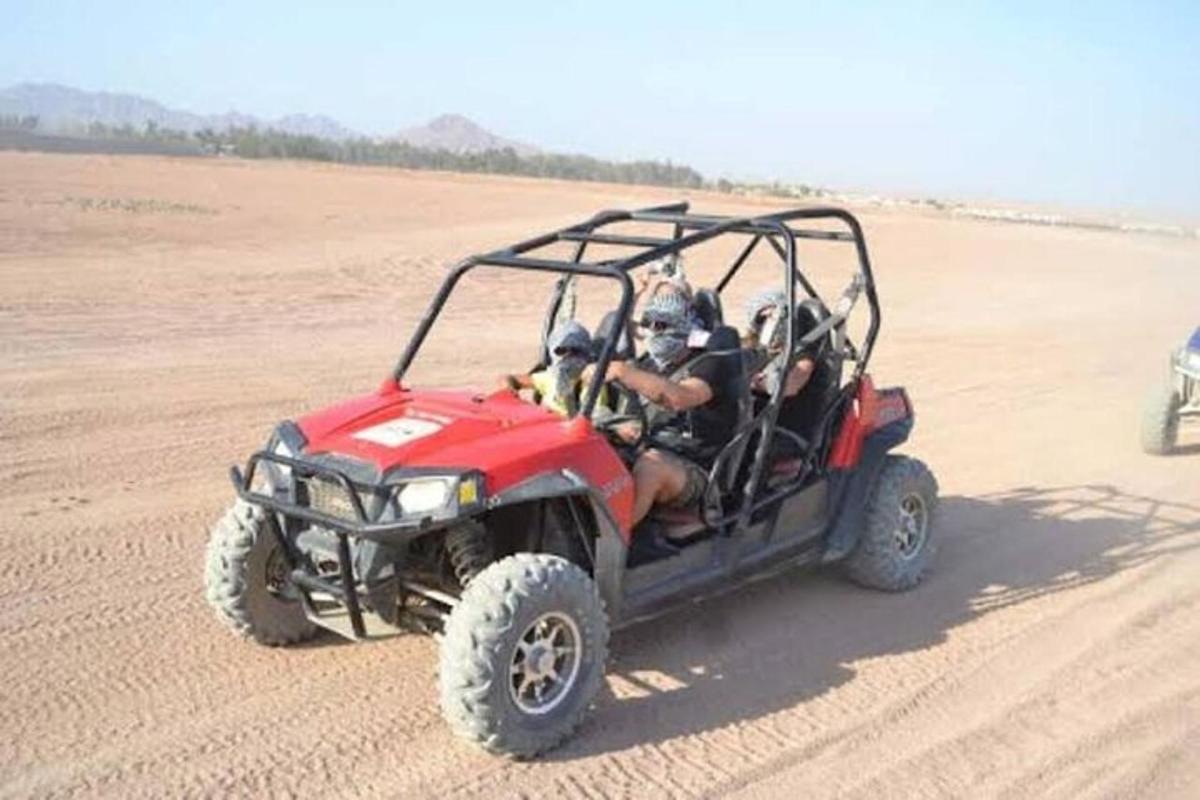 sekumpulan orang menaiki atv merah di padang pasir