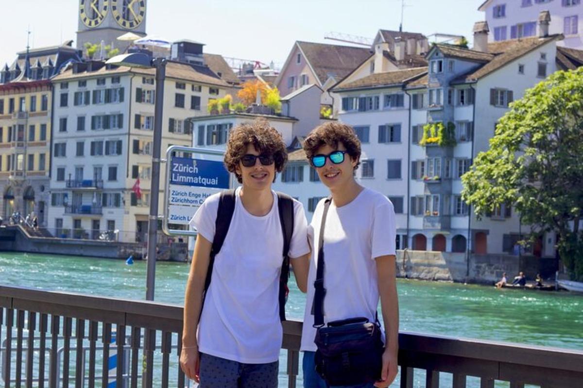 two young men standing next to a river with buildings
