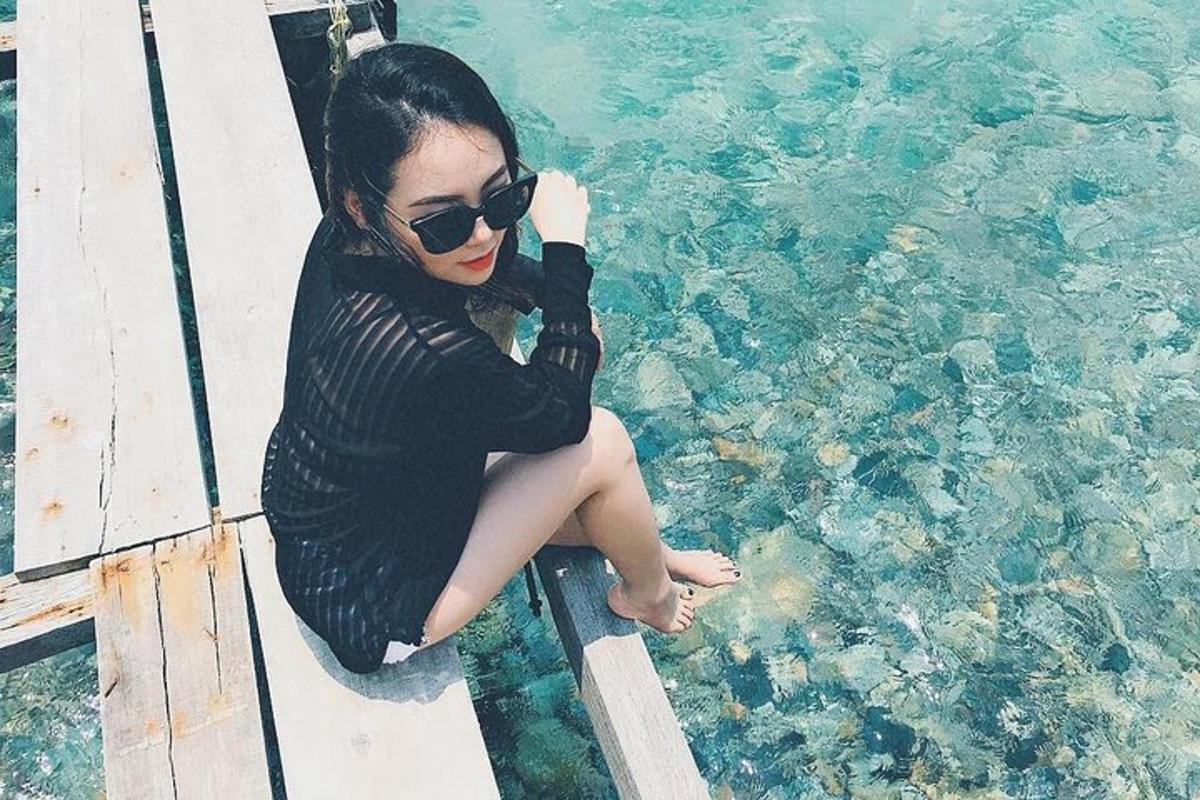 seorang wanita berkacamata hitam duduk di dermaga di samping air