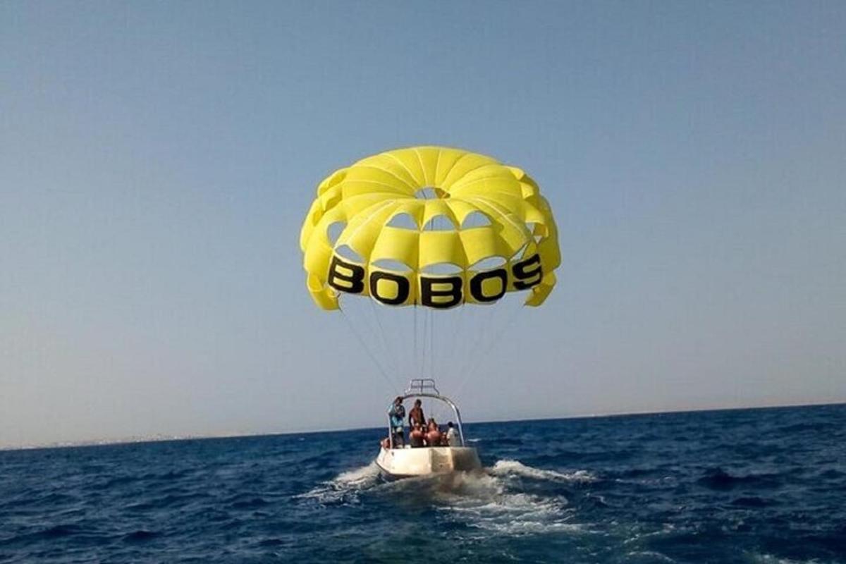 Un paracaídas amarillo volando sobre el agua con gente en un bote.