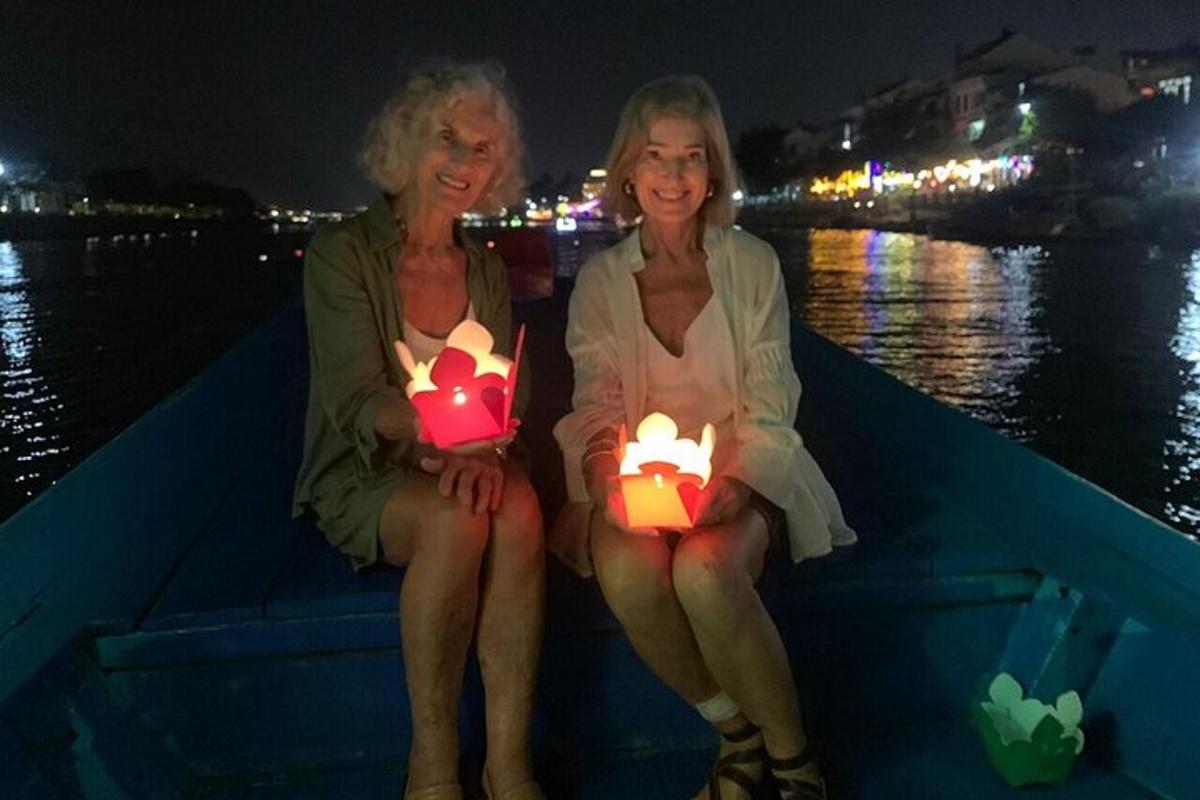 due donne sedute su una barca che tengono in mano candele accese