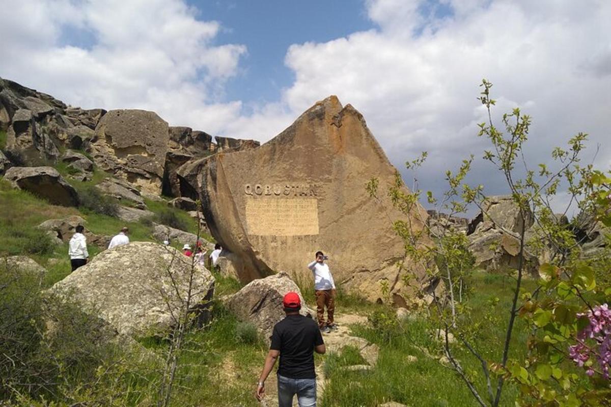 people walking on a trail near a large rock