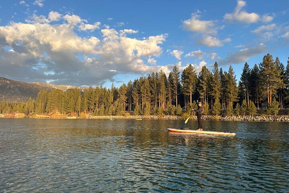un home dret sobre una taula de paddle surf en un llac