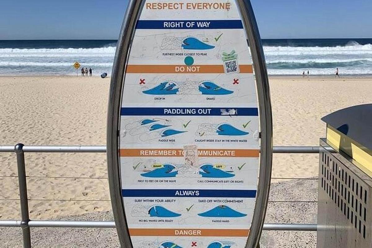 un semn în fața unei plaje cu o placă de surf