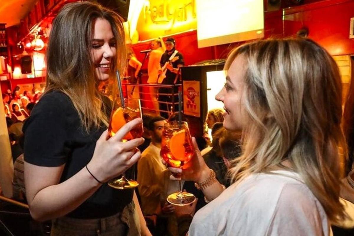 Tvær konur standa á bar og halda á vínglösum