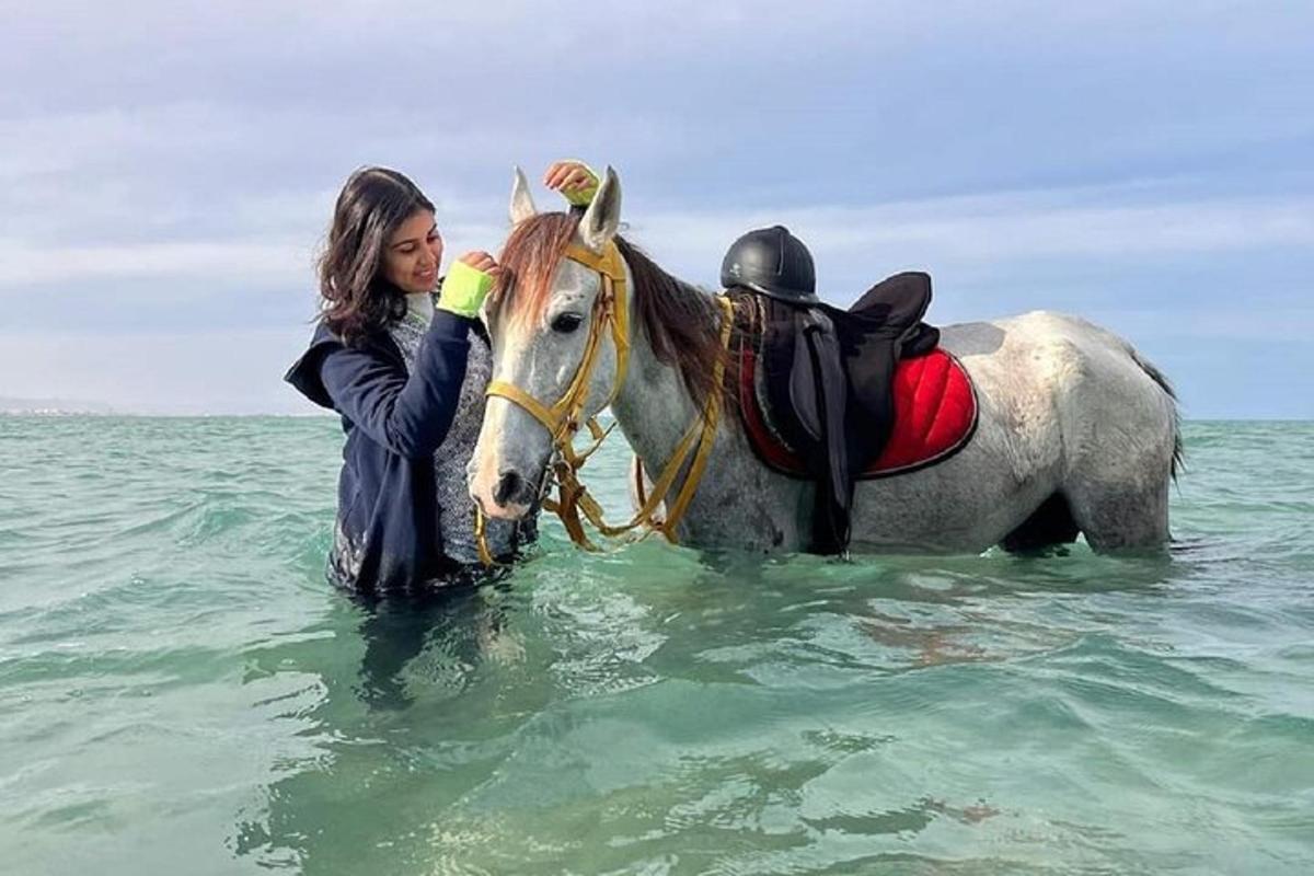 una donna in piedi accanto a un cavallo nell'oceano