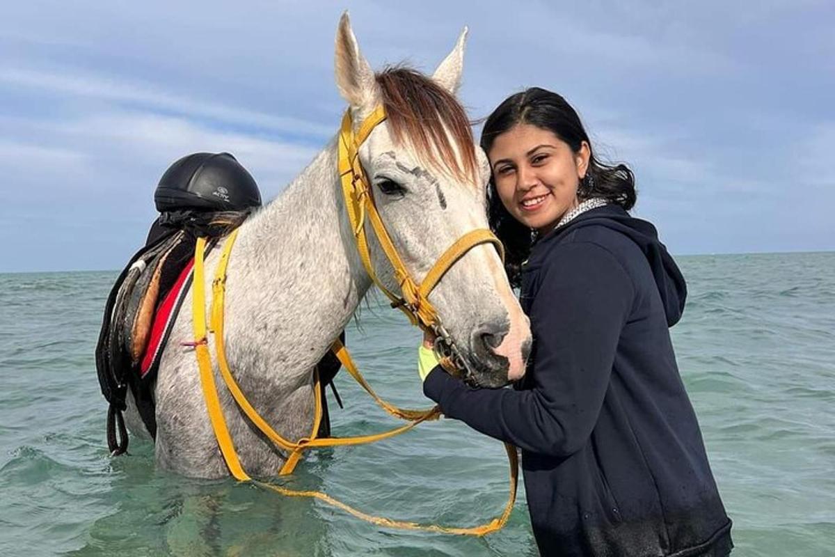 una donna in piedi accanto a un cavallo nell'oceano