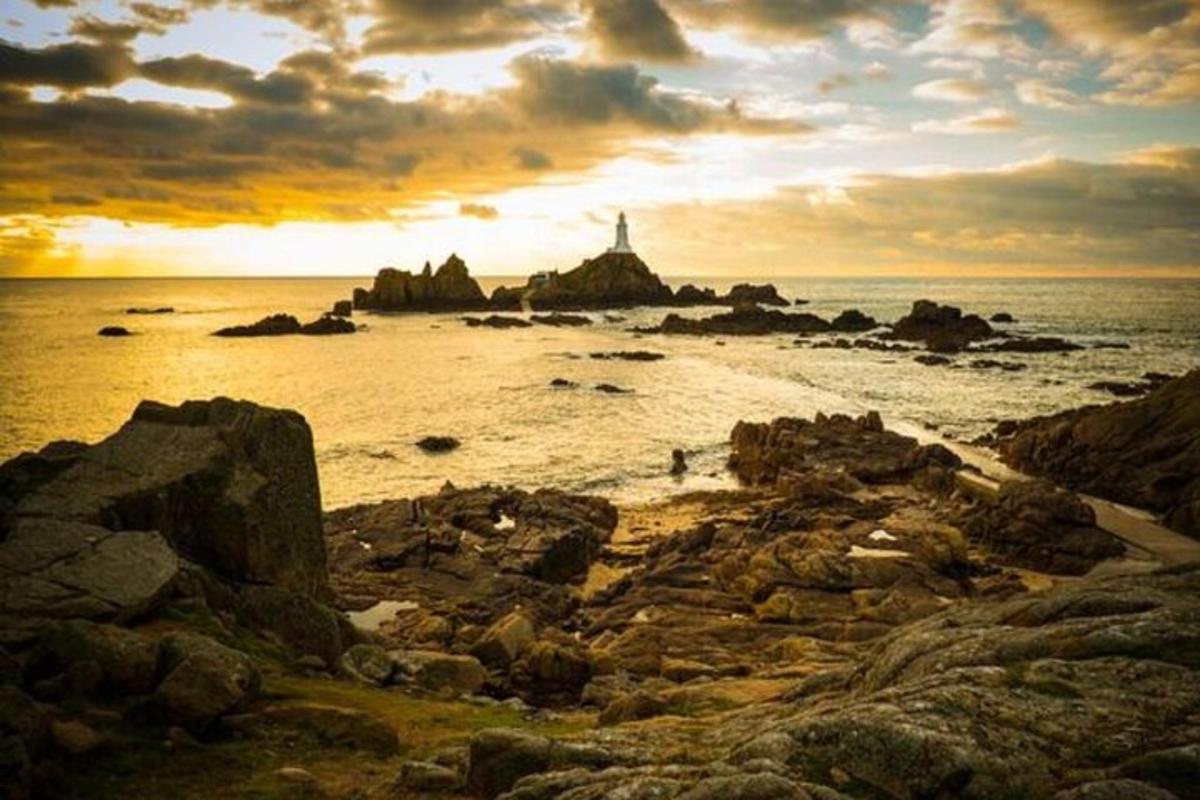 a sunset over a beach with a lighthouse and the ocean
