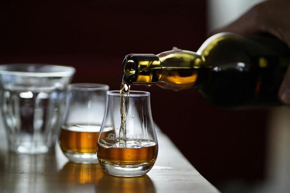seseorang menuangkan alkohol ke dalam gelas di atas meja