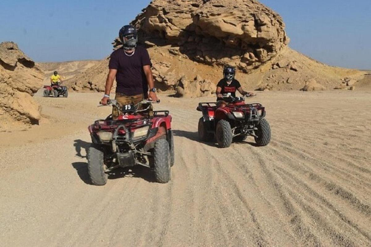 seorang pria berdiri di samping dua ATV di padang pasir