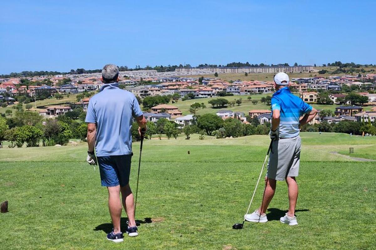 két ember áll egy golfpályán, nézi a várost