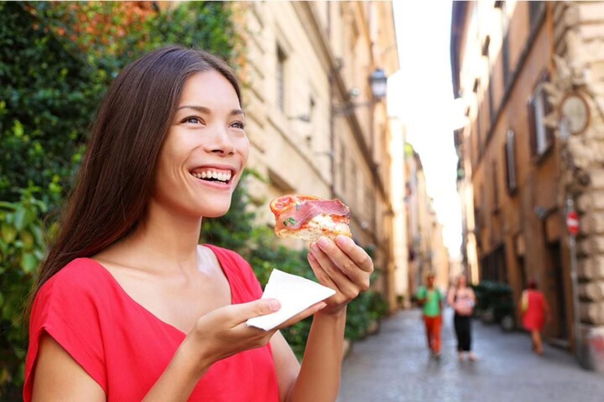 isang babaeng kumakain ng isang slice ng pizza sa isang kalye