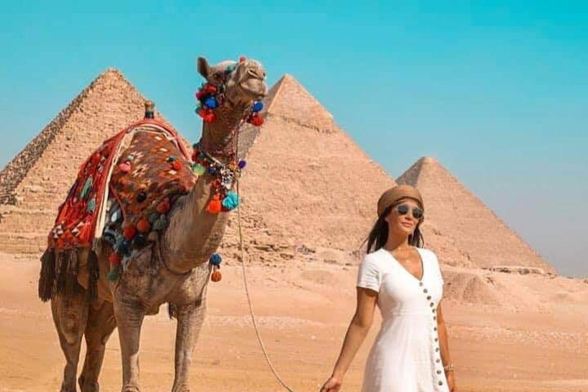 a woman standing next to a camel in front of pyramids