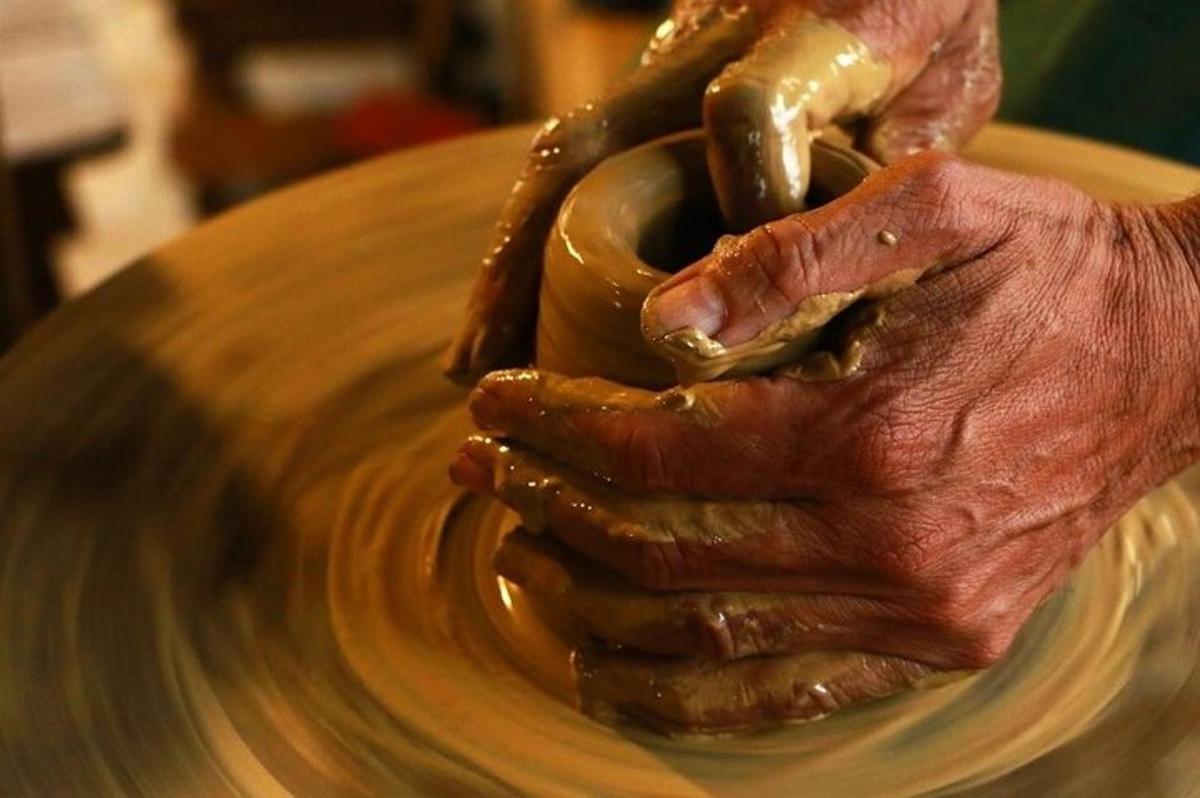 زوج من الأيدي يصنعان وعاءً على عجلة الفخار