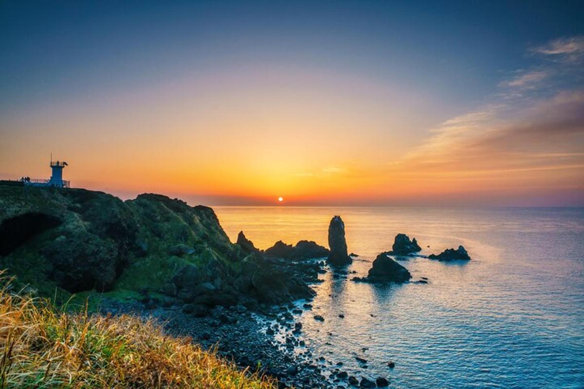 a sunset over the ocean with rocks and a lighthouse