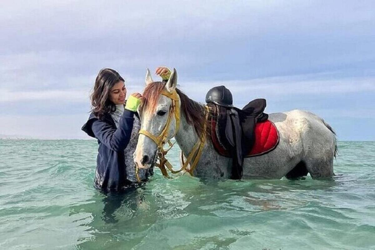 žena stojící vedle koně v oceánu