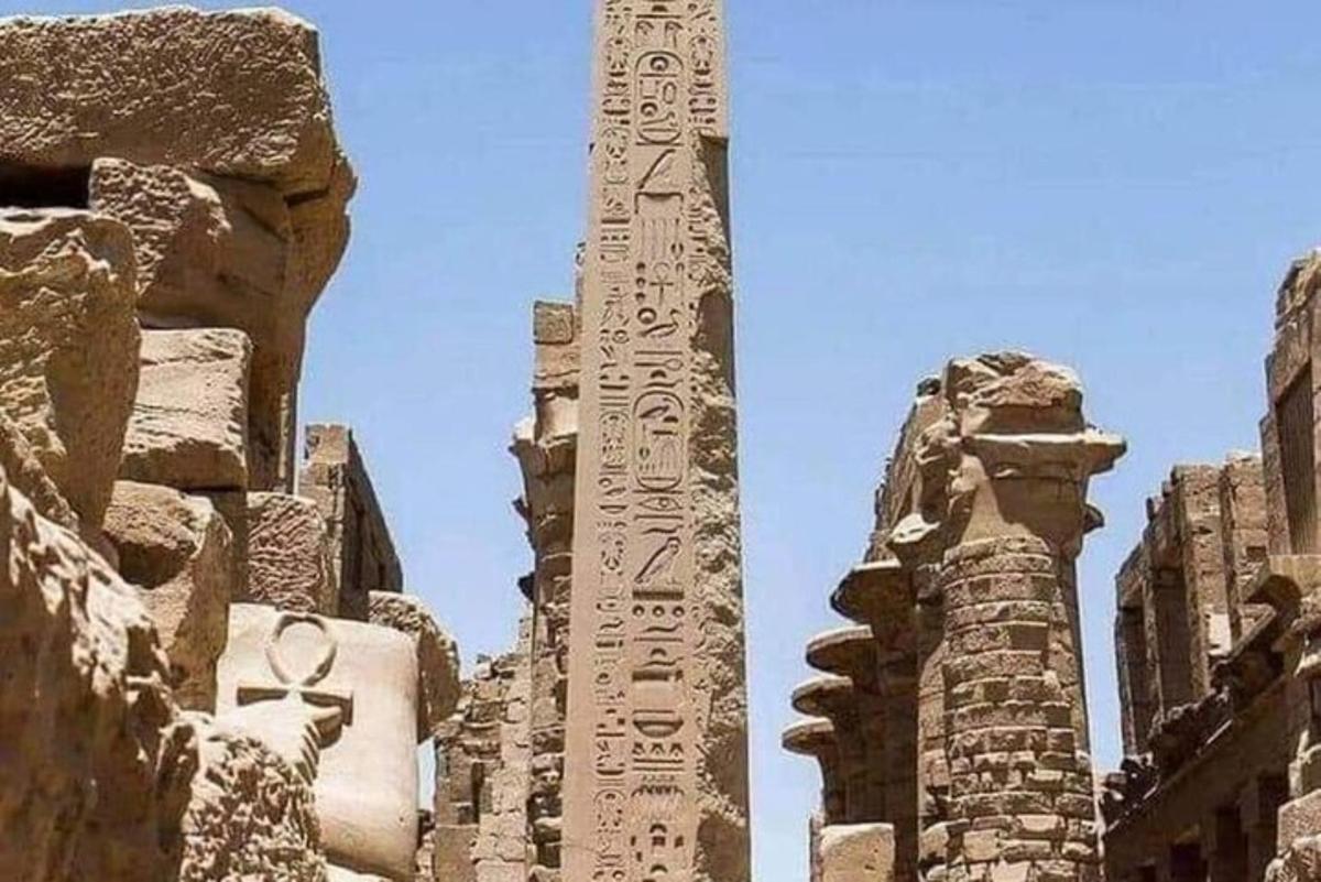 Un obelisco alto en un edificio al lado de una estatua.